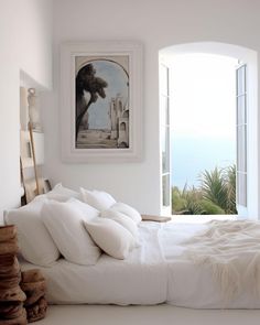 a bed with white sheets and pillows in front of an open window that looks out onto the ocean