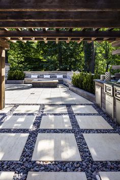 an outdoor kitchen and seating area with stone tiles on the floor, surrounded by trees