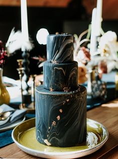 a black and gold wedding cake sitting on top of a wooden table next to candles