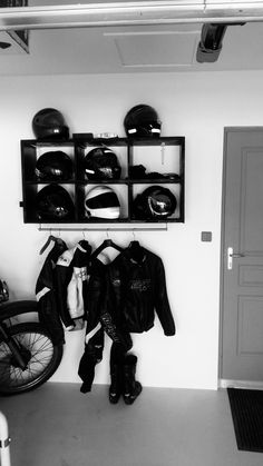 a motorcycle is parked in front of a wall mounted helmet rack with two jackets on it