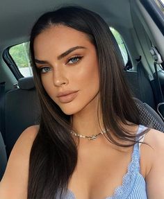 a woman sitting in the back seat of a car wearing a blue top and necklace