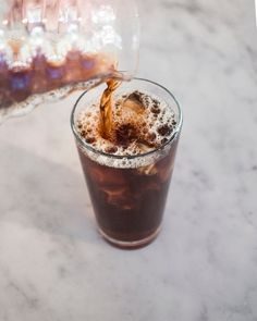 someone pouring coffee into a glass on top of a marble table with white and gray speckles