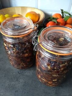 two jars filled with food sitting on top of a counter next to oranges and lemons