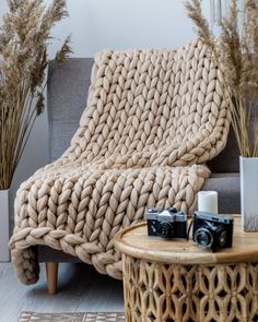 a chair with a blanket on it next to a table and some plants in the background