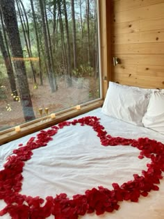 a heart made out of red flowers on a bed in front of a large window