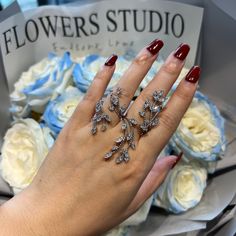 a woman's hand with two rings on it and flowers in the back ground