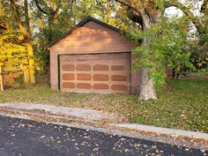 a wooden garage sitting next to a tree in the middle of a park with leaves on the ground