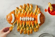 a football shaped pastry on top of a marble table with dipping sauces next to it