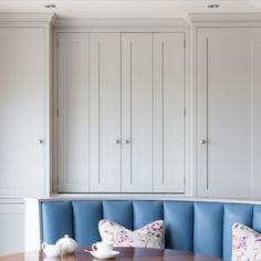 a corner bench with pillows on it in front of white cupboards