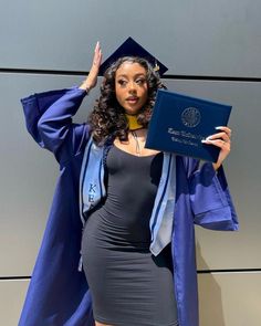 a woman in a graduation gown holds up her diploma while posing for the camera with one hand on her head