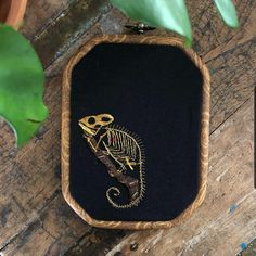 a small black and gold embroidered pouch with a lizard on it's side, sitting next to a potted plant