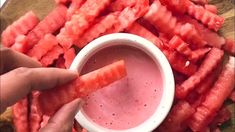 someone is dipping something into a small white bowl filled with watermelon cubes