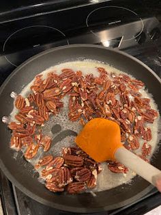 pecans being cooked in a skillet on the stove with an orange spatula