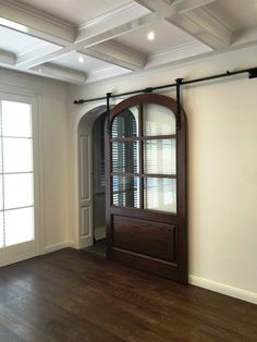 an empty room with a large wooden door and white walls, hardwood floors, and windows