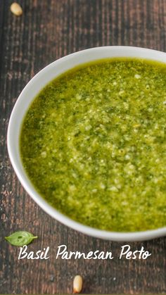 a white bowl filled with green pesto on top of a wooden table next to nuts