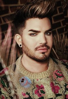 a close up of a person wearing a sweater and piercings on his ear with a brick wall in the background