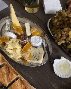 an assortment of cheeses and crackers on a silver platter next to bread