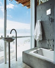 a bath tub sitting under a window next to a sink in a room with large windows