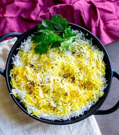 a pan filled with rice and parsley on top of a table next to a pink towel