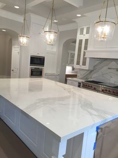 a large kitchen with white cabinets and marble counter tops, lights hanging from the ceiling