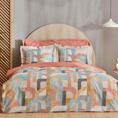 a bed with an orange and blue comforter on it next to a night stand