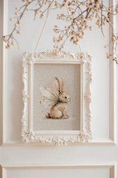 a white frame hanging on the wall with a painting of a bunny in it's lap