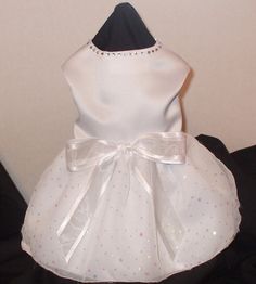 a white dress that is sitting on top of a black cloth bag with a bow at the waist