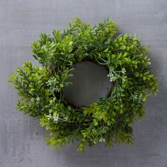 a green wreath hanging on the side of a wall next to a gray wall with white flowers