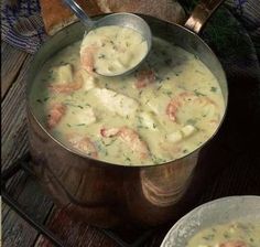 two silver pans filled with shrimp and cheese soup on top of a wooden table