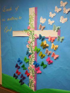 a bulletin board with paper butterflies on it and a cross in the middle that says each of us matters to god