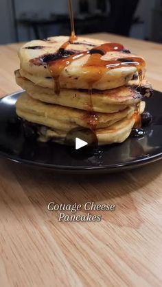 a stack of pancakes on a black plate with syrup drizzled over them