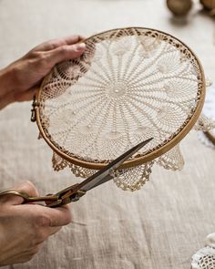 two hands are holding a piece of lace and scissors on a table with doily