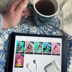 someone is holding an ipad with several movie covers on it and there are two cups of coffee in front of them