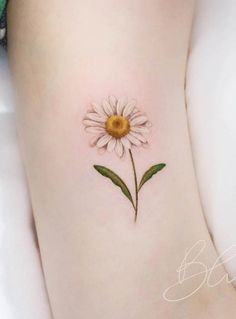 a small daisy tattoo on the side of a woman's leg with green leaves