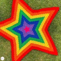 a multicolored crocheted star is laying on the grass in front of it