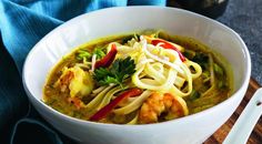 a white bowl filled with noodles and shrimp on top of a wooden cutting board next to chopsticks