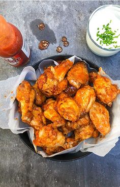 chicken wings in a black bowl next to some dipping sauces and a bottle of ketchup