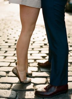 the legs of two people standing next to each other on a cobblestone road