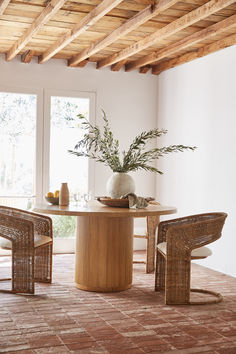 a table with chairs and a vase on top of it in a room that has large windows