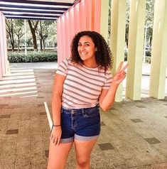 a woman is standing in front of columns and posing for the camera with her hand up