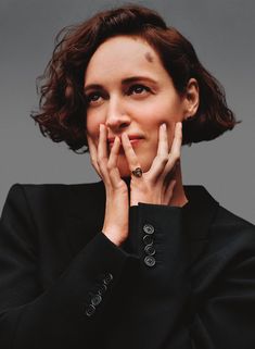 a woman with her hands on her face and wearing a black jacket, posing for the camera