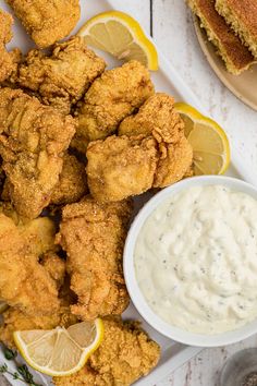 some fried food is on a plate with lemon wedges and sauce next to it