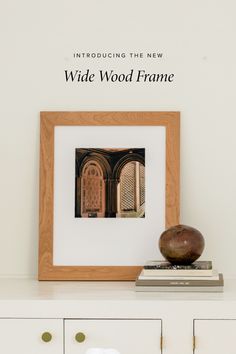 a wooden frame sitting on top of a white dresser next to a vase and books