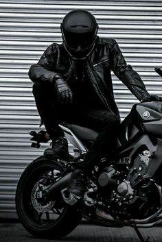 a man sitting on the back of a motorcycle in front of a garage door wearing a black leather jacket