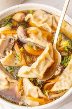 a bowl filled with dumplings and broccoli on top of a white table