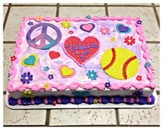 a decorated cake with peace, love, and softballs on it sitting on a tile floor