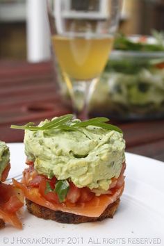 a bottle of wine sitting next to a sandwich on top of a white plate with tomatoes and guacamole