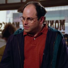 a man wearing glasses standing in front of a store window with his hand on his hip