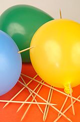 three balloons with pins sticking out of them on an orange tablecloth, one blue and one green