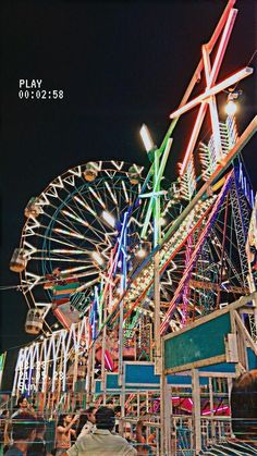 an amusement park at night with ferris wheel in the foreground and people sitting on benches